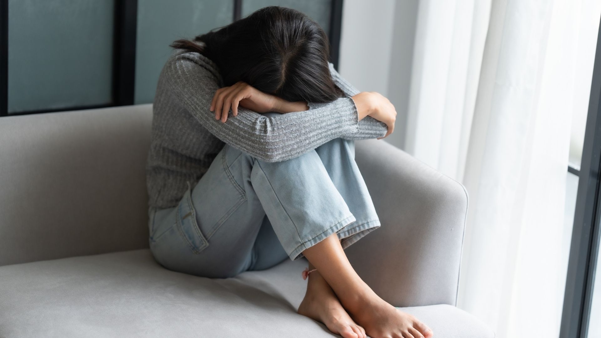 Mujer con la cabeza entre los brazos, sentada en un sofá
