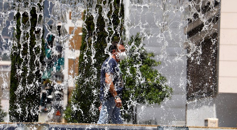 un hombre pasea con mascarilla cerca de una fuente